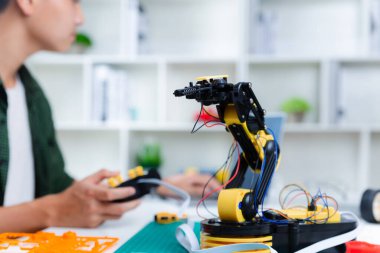 Asyalı genç evde dizüstü bilgisayarla robot kolu ödevi yapıyor. Robot programlama teknolojisi ve BTMM eğitim konsepti.