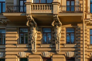 19. yüzyılın sonlarında, güneşli bir günde, Rusya 'nın St. Petersburg kentinde Griboyedov Kanalı' nın setindeki yerleşim yerinin balkonunu destekleyen Atlantisli figürler görülüyor.