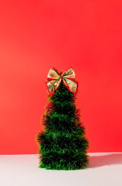 Pastel kırmızı arka planda altın yaylı yeşil Noel ağacının minimum bileşimi. Yeni yıl konsepti. Boşluğu kopyala.