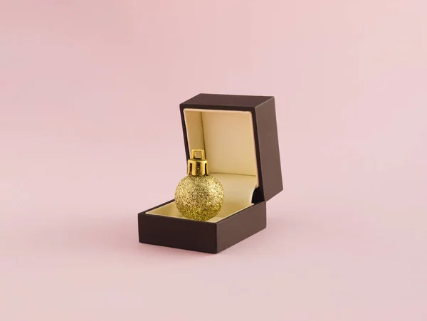 Alyans kutusu ve pastel pembe arka planda parlak altın Noel süsü olan yaratıcı romantik bir tarz. Mutlu yıllar..