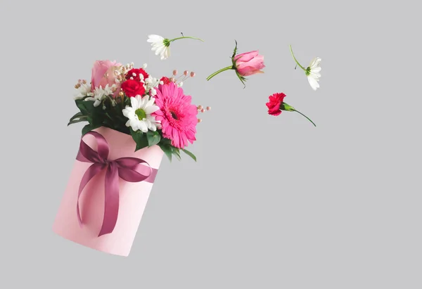Pink gift box with various flowers on grey background. Flying flowers from the box. Valentines day aesthetic nature concept. 8 March card idea.