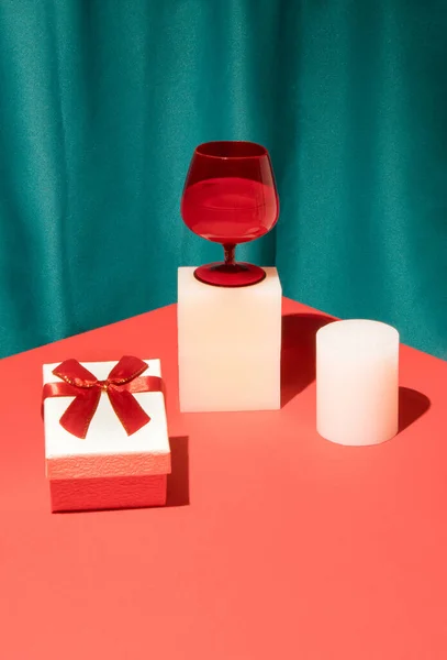 赤ワイングラス ギフトボックスと明るい赤のテーブルの上に製品を表示するレトロなスタイルのシーン 絹の緑のカーテンの背景 最小限のヴィンテージスタイル バレンタインデーパーティーのコンセプト — ストック写真