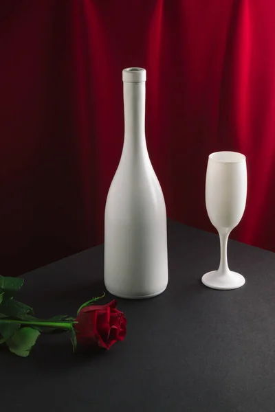 Şarap şişesi, cam ve kırmızı gül çiçekli asgari kalitede bir konsept. Kırmızı perde arkaplanı. Retro Sevgililer Günü partisi konsepti.