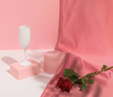 Romantik pastel pembe sevgililer günü kompozisyonu şarap kadehleri, saten perdeler ve kırmızı gül çiçekleri. Ürün Gösterimi ve İş Konsepti için uygundur. Modern estetik.