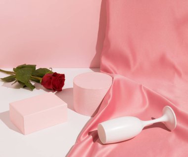 Romantik pastel pembe sevgililer günü kompozisyonu şarap kadehleri, saten perdeler ve kırmızı gül çiçekleri. Ürün Gösterimi ve İş Konsepti için uygundur. Modern estetik.