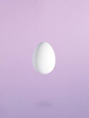 Asgari Paskalya kompozisyonu, pastel mor arka planda havada duran beyaz yumurta..