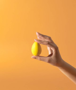 Turuncu arka planda sarı yumurtayı tutan güzel bir kadın. Retro estetik stil. Yaratıcı Paskalya kompozisyonu.