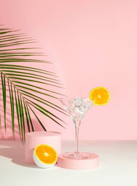 Buzlu ve portakal meyveli martini bardağı, pembe arka planda tropikal palmiye yaprağı ve podyum. Yaz içkisi konsepti çok az. Ürün Gösterimi ve İş Konsepti İçin Uygun.
