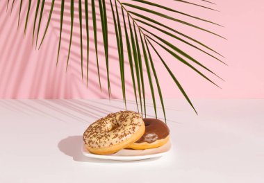 Tropikal palmiye yaprağı ve üzerine de pastel pembe arka planda çikolata konmuş çörekler. En az gıda konsepti.