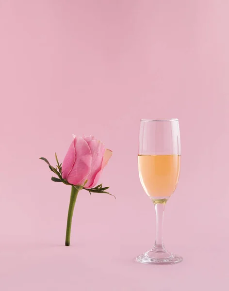 Wine glass and pastel pink rose flower on pink background. Spring minimal concept. Copy space.