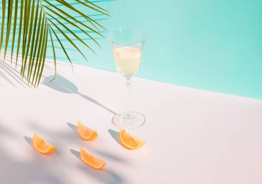 Taze meyve suyu, portakal dilimleri ve mavi arka planda yeşil palmiye dallarıyla yaratıcı bir yaz kompozisyonu. Yaz, tropikal, taze kokteyl konsepti.