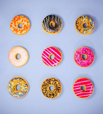 Mor arka planda izole edilmiş 9 farklı renkli çörek seti. Jöleli, çikolatalı, şekerli, soslu, şekerli, fındıklı. En az gıda konsepti.