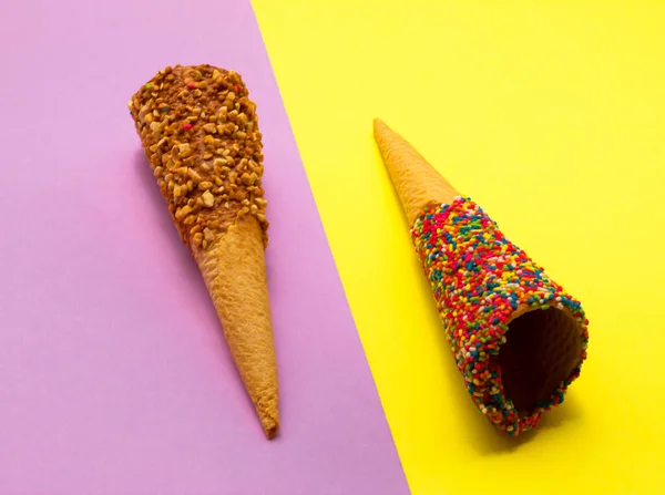 Pastel mor ve sarı arkaplanlı fındıklı renkli dondurma külahları. En düşük yaz kompozisyonu.