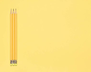 Wooden pastel yellow pencils with erasers on yellow background. Back to school concept. Monochromatic composition with copy space. Top view, flat lay.