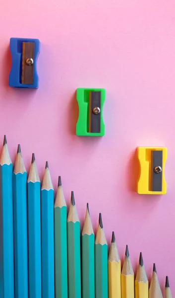Renkli tahta kalemler ve pembe arka planda kalem açacağı. Üst manzara, düz yatış. Okula dönmek, eğitim kavramı..