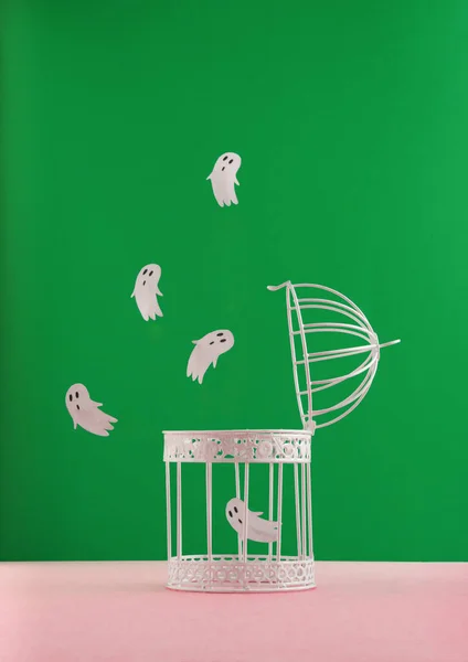 Halloween concept with bird cage and ghosts on pastel pink and green background. Scary and spooky concept. Modern aesthetic.