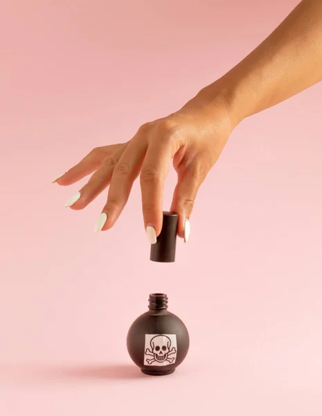 パステルピンクの背景に黒いボトルに赤い爪と毒を持つ女性の手 ハロウィン超現実的な不気味なアイデア — ストック写真