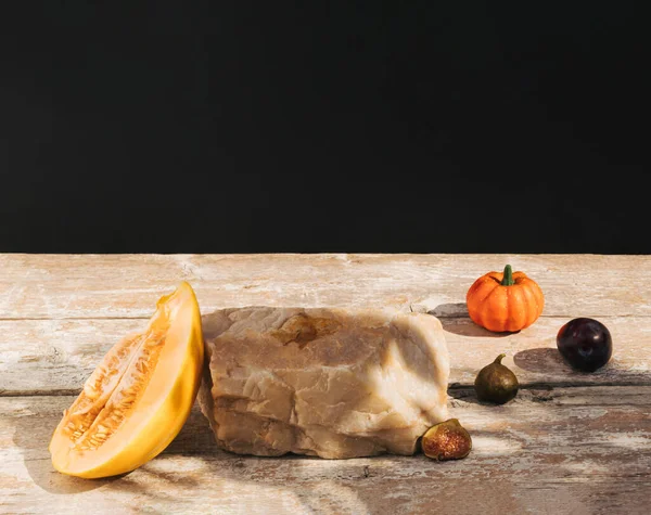 Retro style composition made of melon fruit, figs, pumpkin and rock on old wooden table. Product podium, suitable for product display. Dark background.