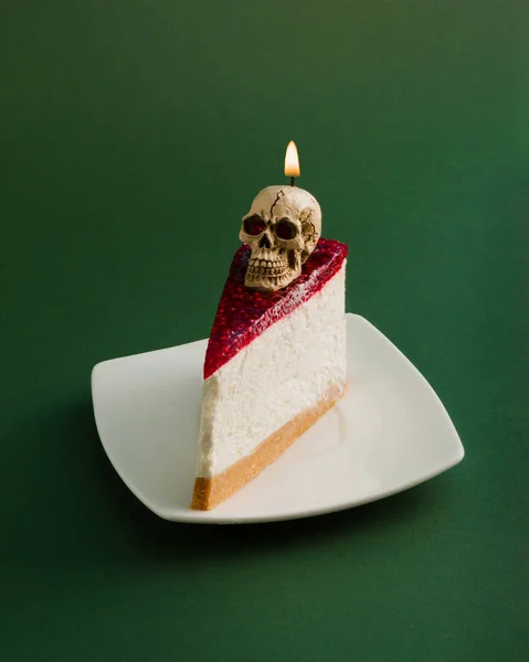 Koyu yeşil arka planda kafatası mumu ve cheesecake ile Cadılar Bayramı minimal konsepti. Ürkütücü ve korkutucu tatil konsepti. Boşluğu kopyala.