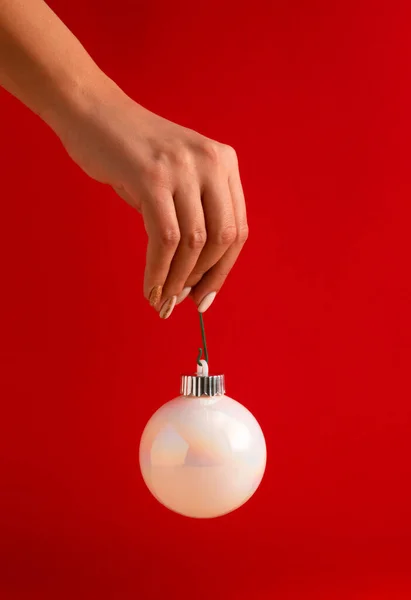 Kırmızı arka planda beyaz, parlak bir Noel mücevheri tutan kadının eli. Minimum tatil konsepti. Mutlu yıllar..