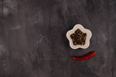 Aromatik renkli biberler yıldız şeklinde bir kabın içinde metalik koyu arkaplanda kırmızı kırmızı acı biberle çevrili. Boşluğu kopyala.