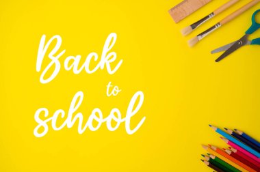 Stationery accessory on yellow background. School supplies, pencils, scissors, brushes and wooden ruler with back to school text on the left side.