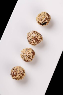 Siyah arka planda beyaz bir tabakta susam tohumlu güzel şekerler.