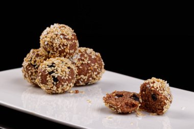 Siyah arka planda beyaz bir tabakta susam tohumlu güzel şekerler.