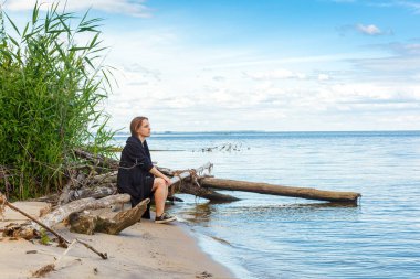 Deniz kıyısında güzel bir kız, mavi gökyüzüne yakından bakıyor.