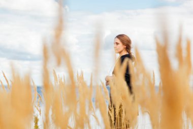 Deniz kıyısındaki bir tarlada güzel bir kız ve bulutlarla çevrili mavi gökyüzü.