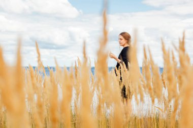 Deniz kıyısındaki bir tarlada güzel bir kız ve bulutlarla çevrili mavi gökyüzü.