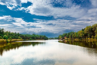Mavi gökyüzü, bulutlar ve yakındaki yeşil ağaçlarla gölün güzel manzarası.