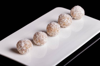 Siyah arka planda beyaz tabakta hindistan cevizli güzel tatlılar.