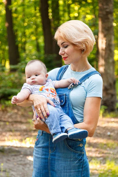 Güzel bir kız, yaz parkında bir çocuğu kollarında tutuyor.
