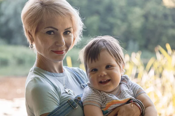 Güzel bir kız gölün arka planında kucağında bir çocuk tutuyor.