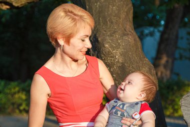 Oğlu olan güzel bir anne yazın parktaki bir ağaca oturur.