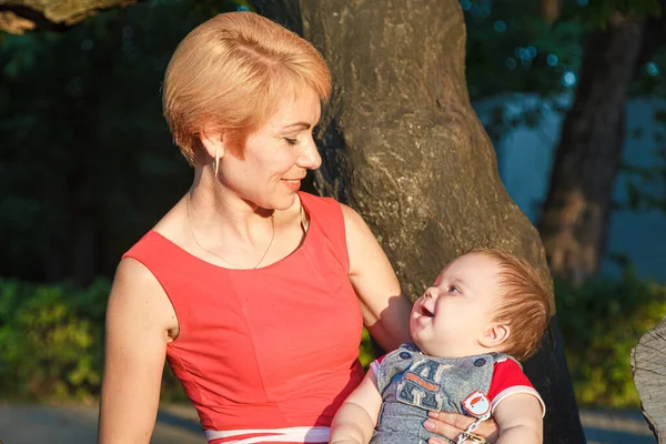 Oğlu olan güzel bir anne yazın parktaki bir ağaca oturur.