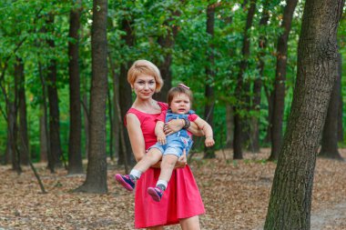 Güzel anne kızıyla birlikte yazın parkta yürür.