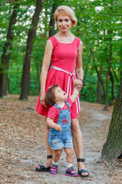 Güzel anne kızıyla birlikte yazın parkta yürür.