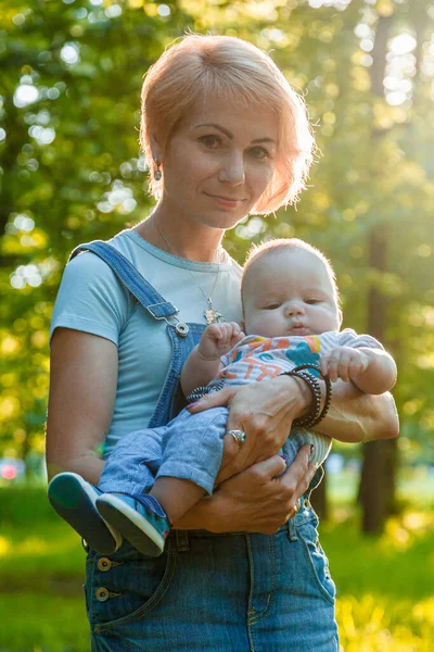 Güzel bir kız, yaz parkında bir çocuğu kollarında tutuyor.