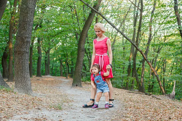 Güzel anne kızıyla birlikte yazın parkta yürür.