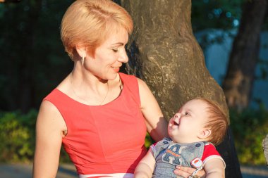 Oğlu olan güzel bir anne yazın parktaki bir ağaca oturur.