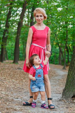 Güzel anne kızıyla birlikte yazın parkta yürür.