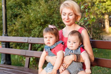 Güzel anne, kızı ve oğluyla birlikte yazın yakın planda bir bankta oturuyor.