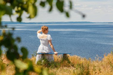Güzel bir kız deniz kenarındaki banklarda oturuyor, gökyüzünü yakından görüyor.