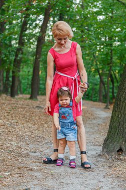 Güzel anne kızıyla birlikte yazın parkta yürür.