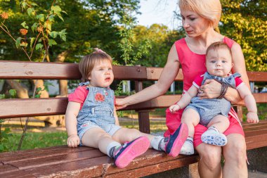 Güzel anne, kızı ve oğluyla birlikte yazın yakın planda bir bankta oturuyor.