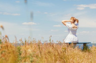 Güzel bir kız deniz kenarındaki banklarda oturuyor, gökyüzünü yakından görüyor.