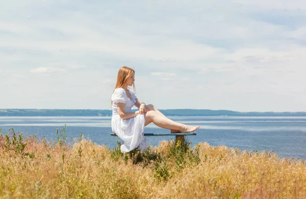 Güzel bir kız deniz kenarındaki banklarda oturuyor, gökyüzünü yakından görüyor.