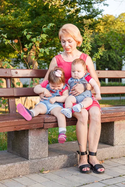 Güzel anne, kızı ve oğluyla birlikte yazın yakın planda bir bankta oturuyor.